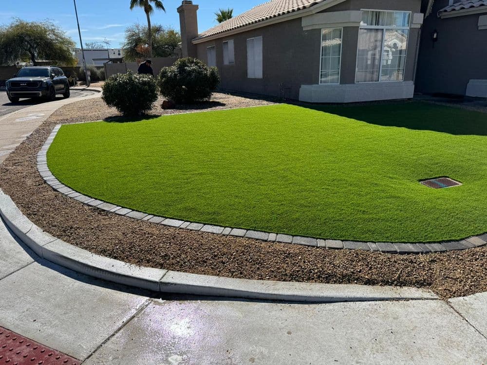 Lush green artificial lawn with stone border in front of a modern house.
